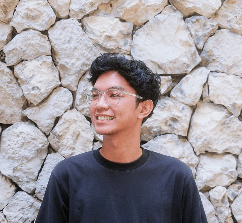 Afnizar smiling in a black sweatshirt against a stone wall